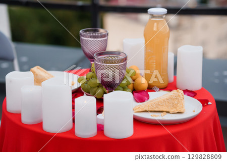 Romantic Rooftop Date Night with Champagne, Fruit Platter, Candles and Red Tablecloth - Intimate Evening Atmosphere. Romantic Rooftop Date Night with Champagne, Fruit Platter, Candles and Red Tablecloth - Intimate Evening Atmosphere. 129828809