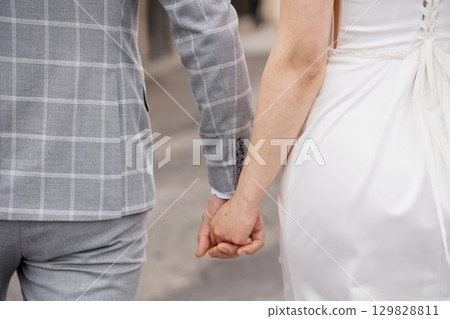 Wedding Couple Holding Hands, Gray Suit, White Dress, Love, Commitment, Formal Attire, Outdoor Scene, Romantic Mood, Stylish Wedding Photography. 129828811