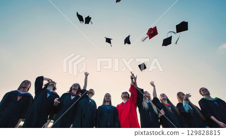 Cheerful graduates celebrate their achievement by throwing their caps in the air with a stunning sunset backdrop 129828815