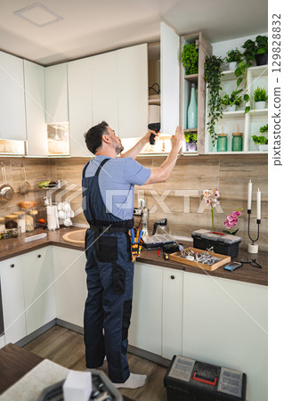 Handyman installing kitchen cabinets using electric screwdriver Handyman installing kitchen cabinets using electric screwdriver 129828832