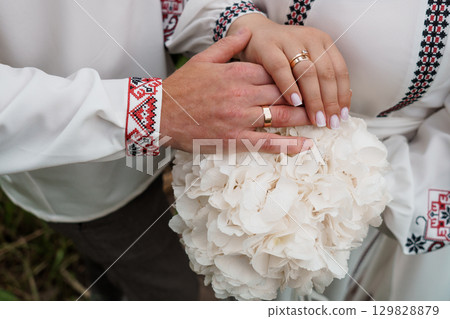 Ukrainian Wedding Hands with Gold Rings and Embroidered Shirts Bouquet, Traditional Culture, White Flowers, Symbolic Love and Celebration Ukrainian Wedding Hands with Gold Rings and Embroidered Shirts Bouquet, Traditional Culture, White Flowers, Symbolic Love and Celebration 129828879