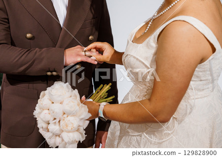 Elegant Wedding Ceremony Exchange: Brown Suit, White Lace Dress, Gold Rings, Bouquet, Pearl Necklace, Romantic Love, Celebration, Indoor Venue, Texture. 129828900