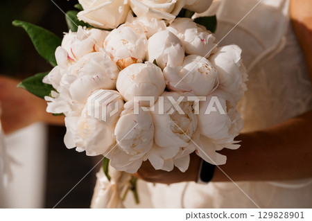 Elegant White Peony Wedding Bouquet Held by Bride in Cream Gown. Close-up Romantic Floral Arrangement, Soft Focus, Delicate Textures. 129828901