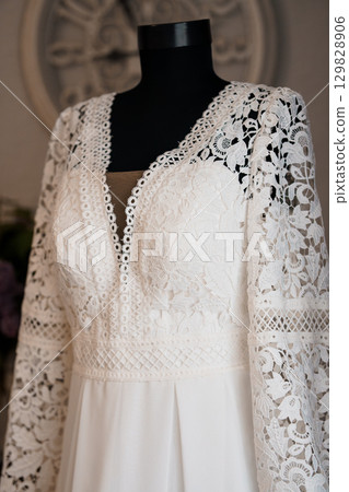 Elegant Ivory Lace Wedding Dress on Mannequin. Detailed Bohemian Gown Close-up. White Textile. Fashionable Bridal Style. Romantic Ceremony Focus 129828906