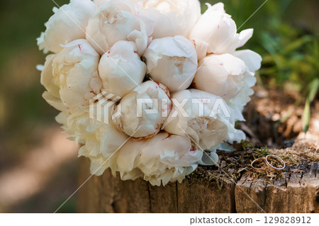 Wedding Peony Bouquet with Rings on Rustic Wood, Romantic Floral Arrangement, White Flowers, Love Symbol, Engagement, Celebration Style. Wedding Peony Bouquet with Rings on Rustic Wood, Romantic Floral Arrangement, White Flowers, Love Symbol, Engagement, Celebration Style. 129828912