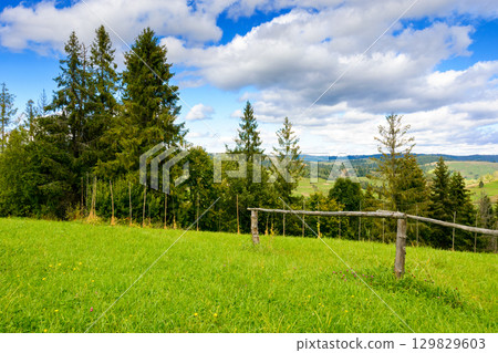 countryside scenery with meadow in mountains. wide rolling rural landscape with wooden fence on green field and forested hills on an autumn afternoon countryside scenery with meadow in mountains. wide rolling rural landscape with wooden fence on green field and forested hills on an autumn afternoon 129829603