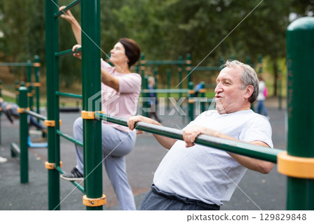 elderly man doing exercises on a horizontal bar at an outdoor sports ground 129829848