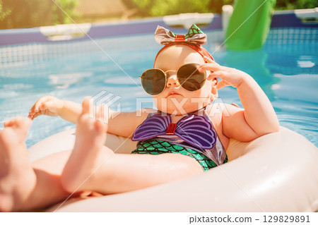Cute Mermaid Baby Girl in Sunglasses Relaxing on Float in Pool on Sunny Day Cute Mermaid Baby Girl in Sunglasses Relaxing on Float in Pool on Sunny Day 129829891