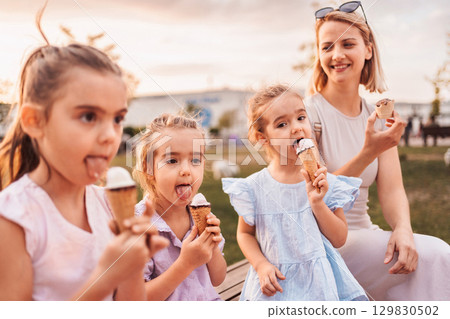 Mother and daughters enjoying ice cream cones in a park 129830502