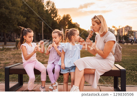 Mother and daughters enjoying ice cream cones in a park at sunset 129830506