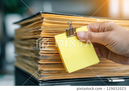 Hand Placing Sticky Note on Document Stack During Validation Process in Office Environment 129832023