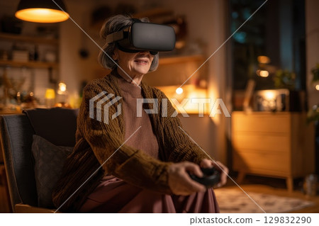 Elderly woman experiencing virtual reality at home with headset and joy on her face 129832290