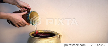 A hand holds a clay jar and pours water A hand holds a clay jar and pours water 129832352