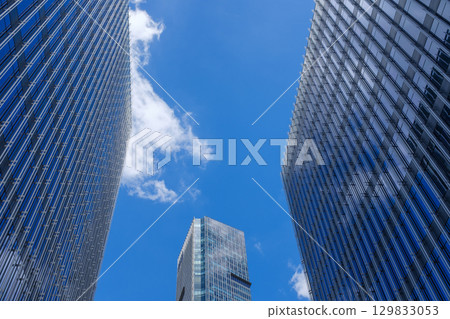 Looking up at the blue sky and white clouds between skyscrapers 129833053