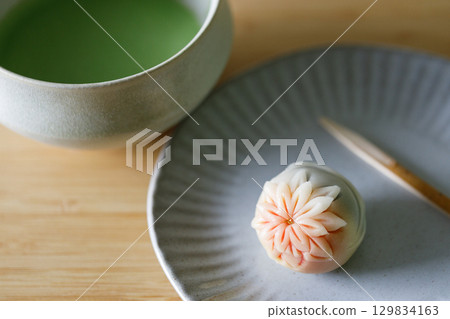 Cup of fresh matcha tea, green tea and Nerikiri, Japanese confectionery, on wooden table. Cup of fresh matcha tea, green tea and Nerikiri, Japanese confectionery, on wooden table. 129834163