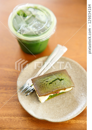 Cup of fresh matcha tea, green tea and Cheese and Matcha and red bean paste financier, small French almond cake, on wooden table. 129834184