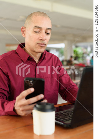 Bald man working on laptop computer at outdoor coffee shop in business or campus setting 129834660