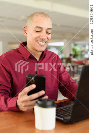 Bald man working on laptop computer at outdoor coffee shop in business or campus setting 129834661
