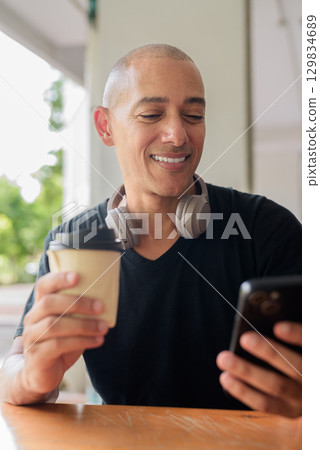 Bald man sitting and smiling while using mobile phone Bald man sitting and smiling while using mobile phone 129834689