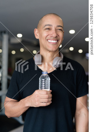 Hispanic bald man athlete in gym drinking water from bottle 129834708