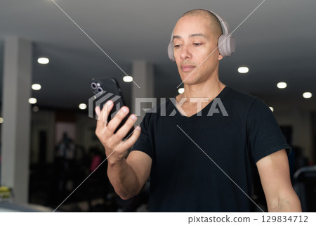 Hispanic bald man athlete in gym using mobile phone 129834712