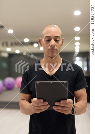 Hispanic bald man athlete in gym classroom using digital tablet computer Hispanic bald man athlete in gym classroom using digital tablet computer 129834724