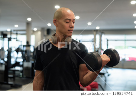 Hispanic bald man athlete in gym doing bicep curl with dumbbell Hispanic bald man athlete in gym doing bicep curl with dumbbell 129834741