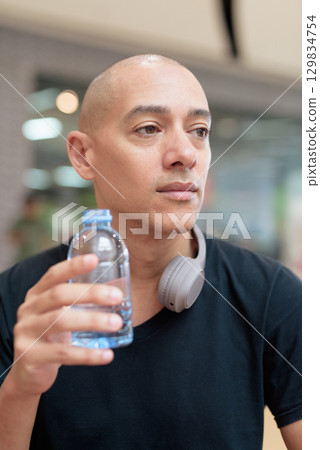 Man drinking water in mall food court, hydration and wellness focus 129834754