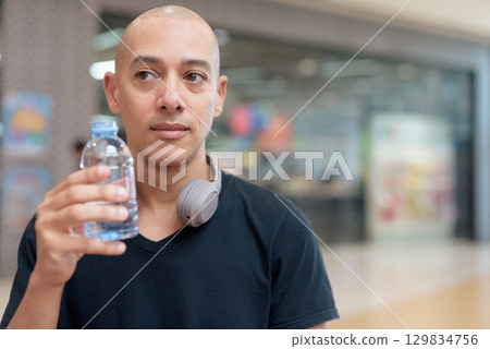 Man drinking water in mall food court, hydration and wellness focus 129834756