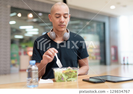 Man eating healthy salad in food court, health and wellness lifestyle 129834767