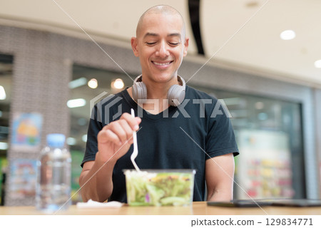 Man eating healthy salad in food court, health and wellness lifestyle Man eating healthy salad in food court, health and wellness lifestyle 129834771