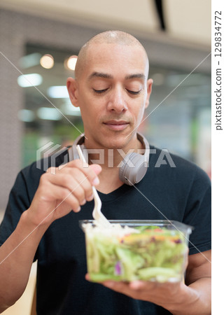 Man eating healthy salad in food court, health and wellness lifestyle 129834772