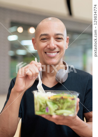 Man eating healthy salad in food court, health and wellness lifestyle 129834774