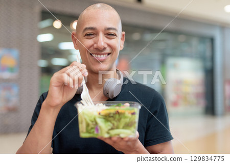 Man eating healthy salad in food court, health and wellness lifestyle 129834775
