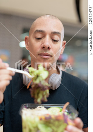 Man eating healthy salad in food court, health and wellness lifestyle 129834784