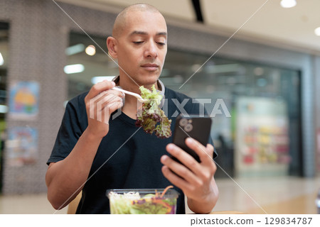 Man eating healthy salad in food court, health and wellness lifestyle Man eating healthy salad in food court, health and wellness lifestyle 129834787