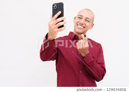 Portrait of man using mobile phone taking selfie against white background 129834808