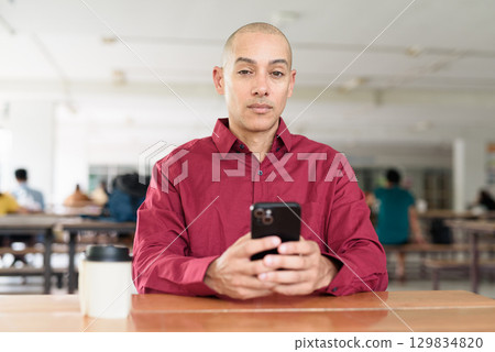 Man using mobile phone at outdoor cafe restaurant in university area with takeaway coffee 129834820