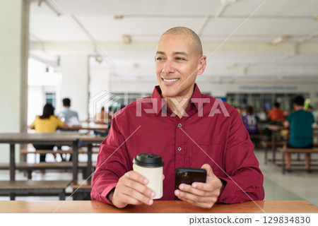 Man using mobile phone at outdoor cafe restaurant in university area with takeaway coffee Man using mobile phone at outdoor cafe restaurant in university area with takeaway coffee 129834830