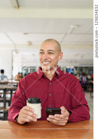 Man using mobile phone at outdoor cafe restaurant in university area with takeaway coffee 129834832