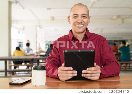 Man using digital tablet computer device at outdoor cafe restaurant table in urban academic setting 129834840