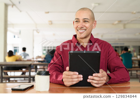 Man using digital tablet computer device at outdoor cafe restaurant table in urban academic setting 129834844
