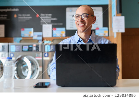 Businessman using laptop in laundry shop, focused and professional working concept Businessman using laptop in laundry shop, focused and professional working concept 129834896