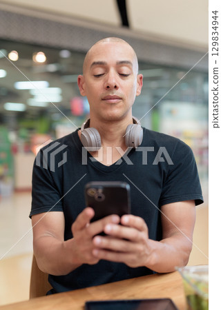 Man using mobile phone and texting in mall food court cafe, digital lifestyle concept 129834944