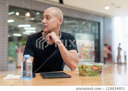 Man using tablet while eating salad in mall, digital lifestyle and wellness Man using tablet while eating salad in mall, digital lifestyle and wellness 129834951