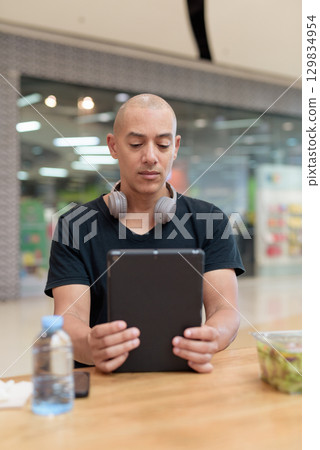 Man using tablet while eating salad in mall, digital lifestyle and wellness Man using tablet while eating salad in mall, digital lifestyle and wellness 129834954