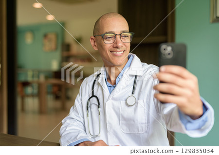 Doctor Sitting Indoors in Clinic or Hospital Area Library with Stethoscope Doctor Sitting Indoors in Clinic or Hospital Area Library with Stethoscope 129835034