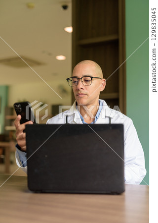 Doctor Sitting Indoors in Clinic or Hospital Area Library Using Laptop Computer 129835045