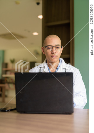 Doctor Sitting Indoors in Clinic or Hospital Area Library Using Laptop Computer 129835046