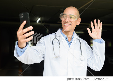 Bald Male Scientist Standing Outside Modern Research Facility Using Phone 129835080